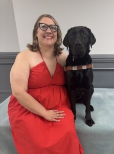 Katie sits close beside black Lab guide dog Fable for their team portrait