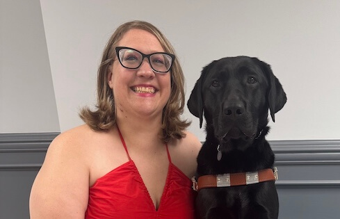 Katie sits close beside black Lab guide dog Fable for their team portrait