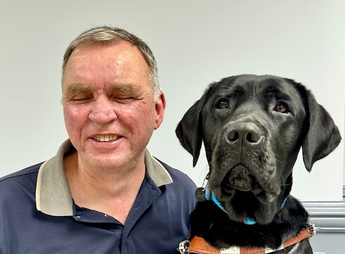 Mel and black Lab guide dog Tarzan sit side by side for their indoor team portrait