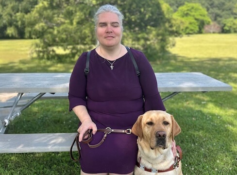 Rebecca sit on the bench of a shaded picnic table for their team portrait