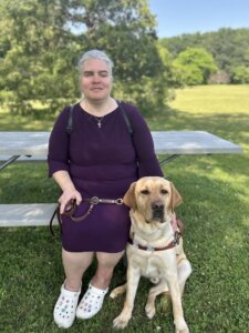 Rebecca sit on the bench of a shaded picnic table for their team portrait