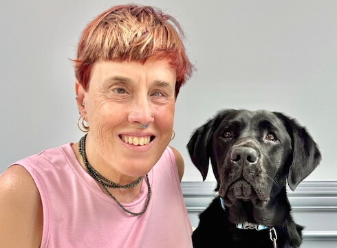 Suzanne sits beside black Lab guide dog Paula for their team portrait