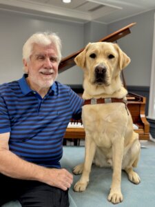 Terry sits beside yellow Lab guide dog Army for their team portrait