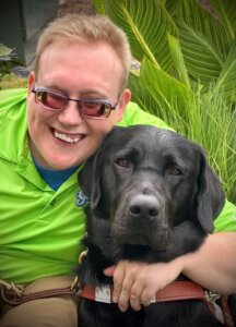Andrew leans in with his arm around black Lab guide Jiminy's neck for their team portrait