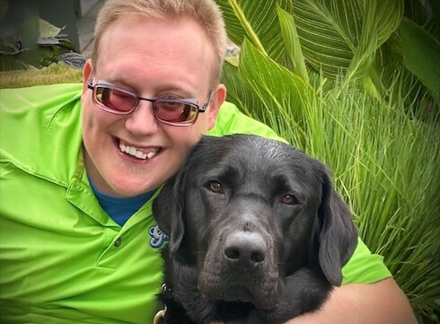 Andrew leans in with his arm around black Lab guide Jiminy's neck for their team portrait