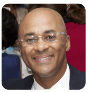 Christopher Perry - new president and CEO -smiles in a 
headshot photo. He is wearing rimless glasses and a dark suit with a
white shirt.