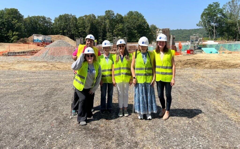 Members of the Client Experience team wear white hard hats and bright yellow vests at the construction site