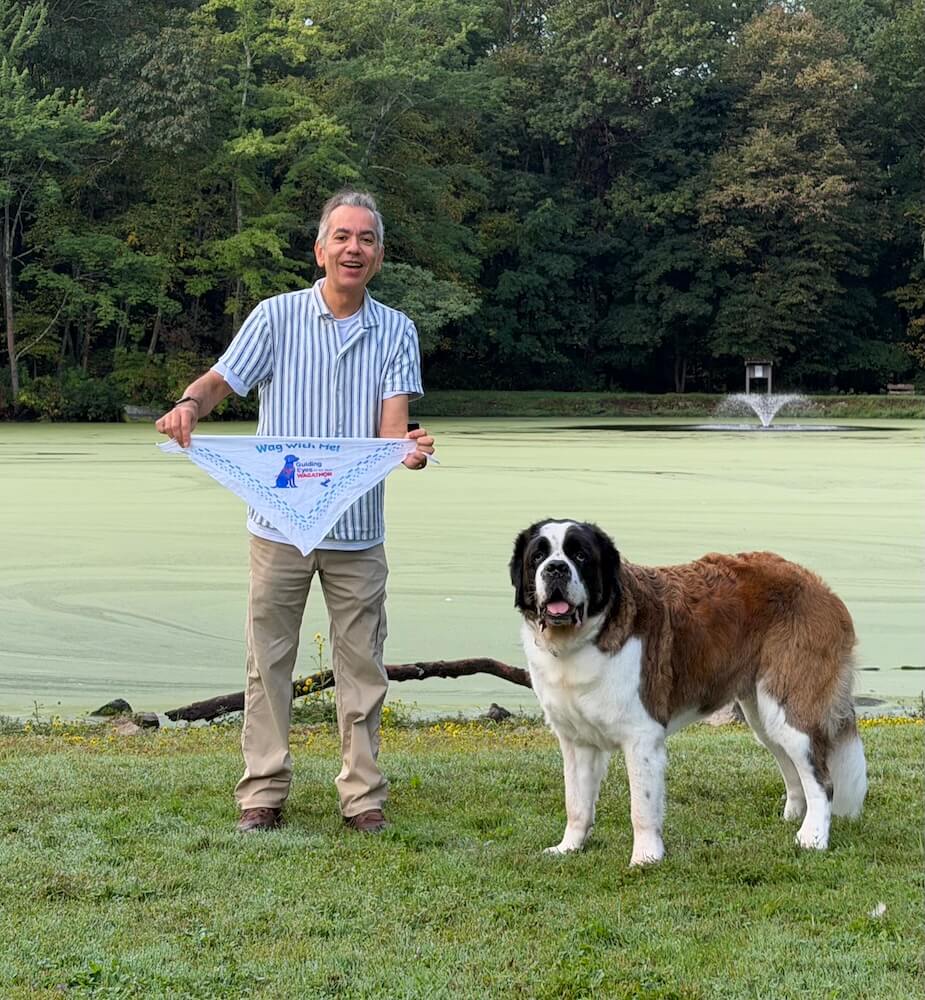 A man holds out a Wagathon bandana while a Saint Bernard stands with him in front of a pond covered in green