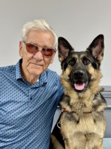 Ted and German Shepherd guide dog Tempo sit indoors for their team portrait