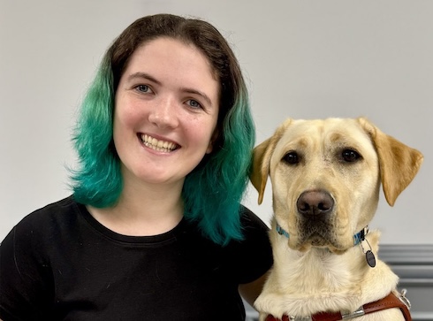 Abby sits beside yellow Lab guide dog Annie, against a gray background, for their team portrait