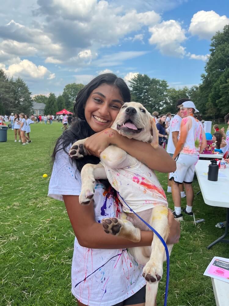 Starter raiser Mira, cuddles yellow puppy Kingdom at an outdoor event
