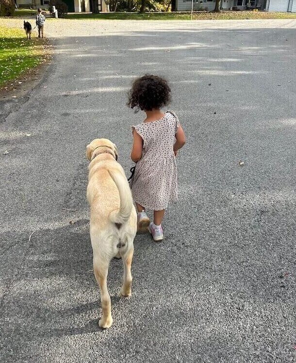 A little girl from the raiser family walks pup Dream down a rural street