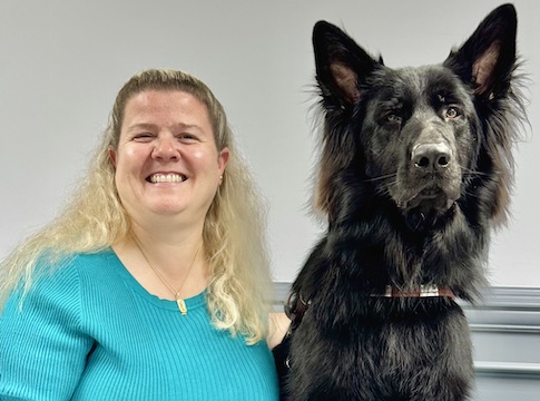 Sharon sits next to her black German Shepherd guide dog Stephen, who's ears tower above for the team portrait.