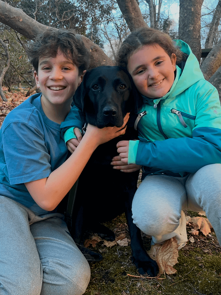 Two children are on either side of Vega, happily posing outside with three heads together.