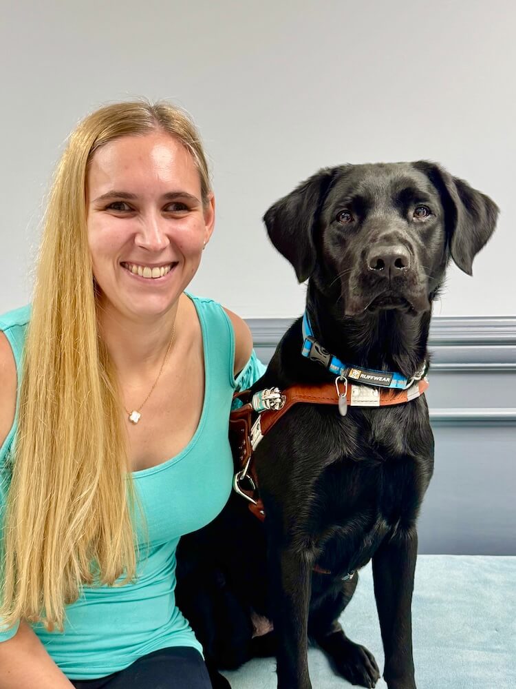 Mikayla and black lab guide dog Tally are sitting for their graduate team portrait