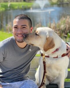 Arturo receives a kiss from yellow Lab guide dog Vangie