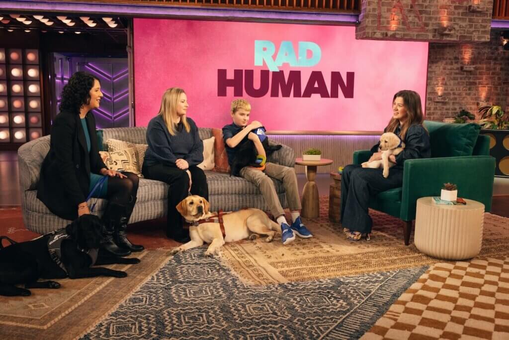 Kelly Clarkson holds a puppy while conversing with Rebekah, Liz and Clark. Rad Human displays on back wall. (Photo by: Weiss Eubanks/NBCUniversal)