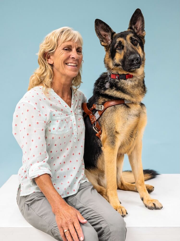 Katie and German Shepherd guide dog Steinway sit side by side for their team portrait against a blue background