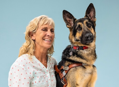 Katie and German Shepherd guide dog Steinway sit side by side for their team portrait against a blue background