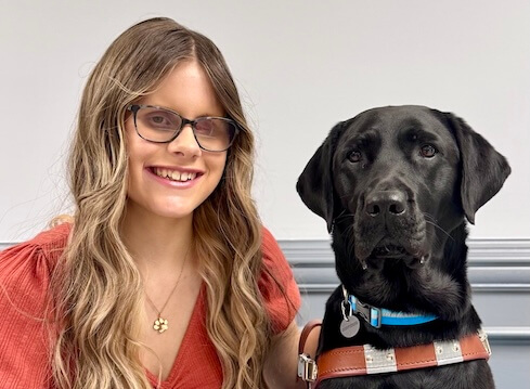 Kelsey and black lab guide dog Java sit against a grey background for their graduate team portrait