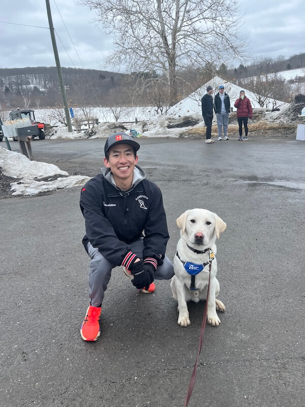 Pup Polar in a Future Guide Dog vest poses with a runner in bright orange-red running shoes