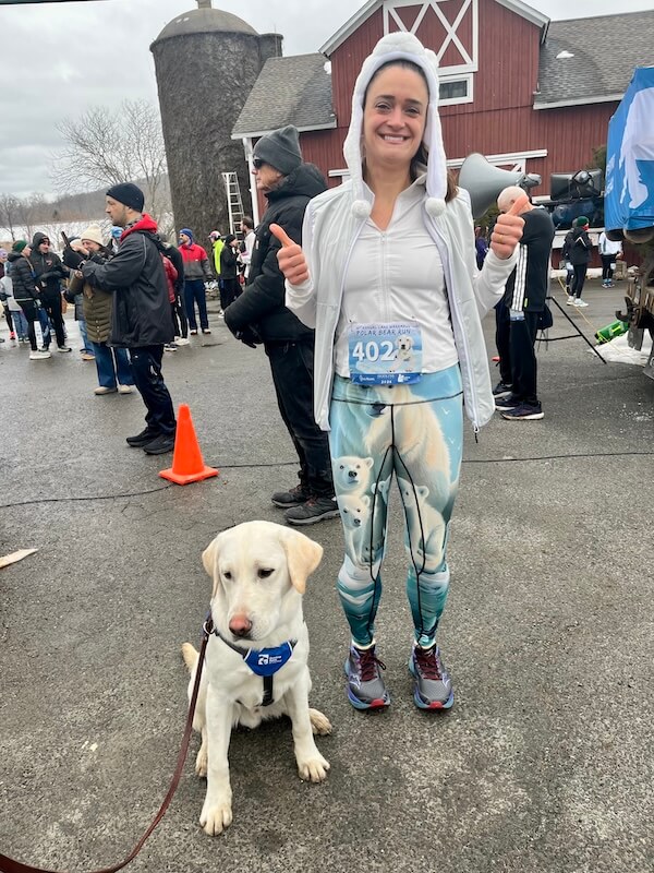 Pup Polar in a Future Guide Dog vest poses with a runner in running attire printed with polar bears