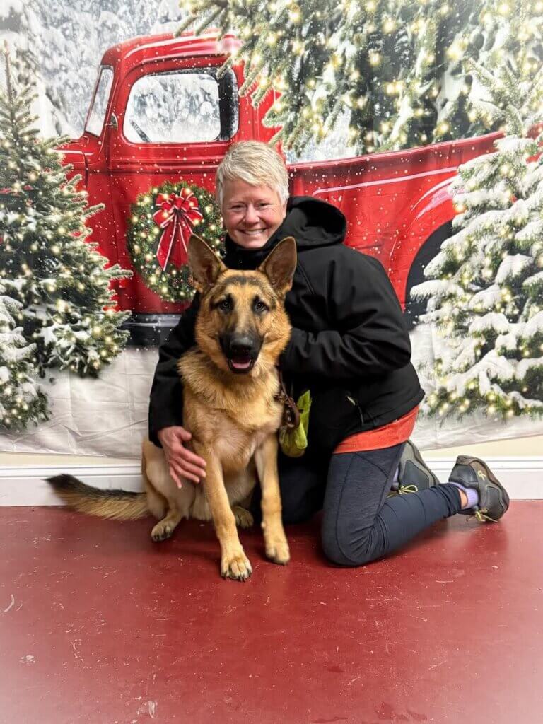 Raiser Missi and German Shepherd pup Usher pose in front of a Christmasy backdrop of evergreens and and vintage red truck
