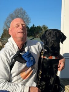 Tommy and black Lab guide dog Fabian sit for their team portrait against a deep blue sky.