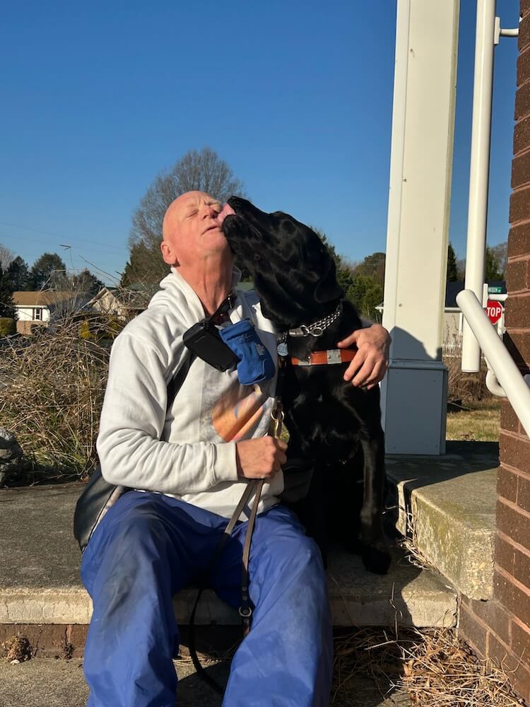 Tommy pulls his head back as his guide Fabian assertively plants a wet kiss across his nose.