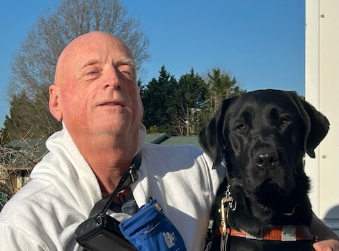 Tommy and black Lab guide dog Fabian sit for their team portrait against a deep blue sky.