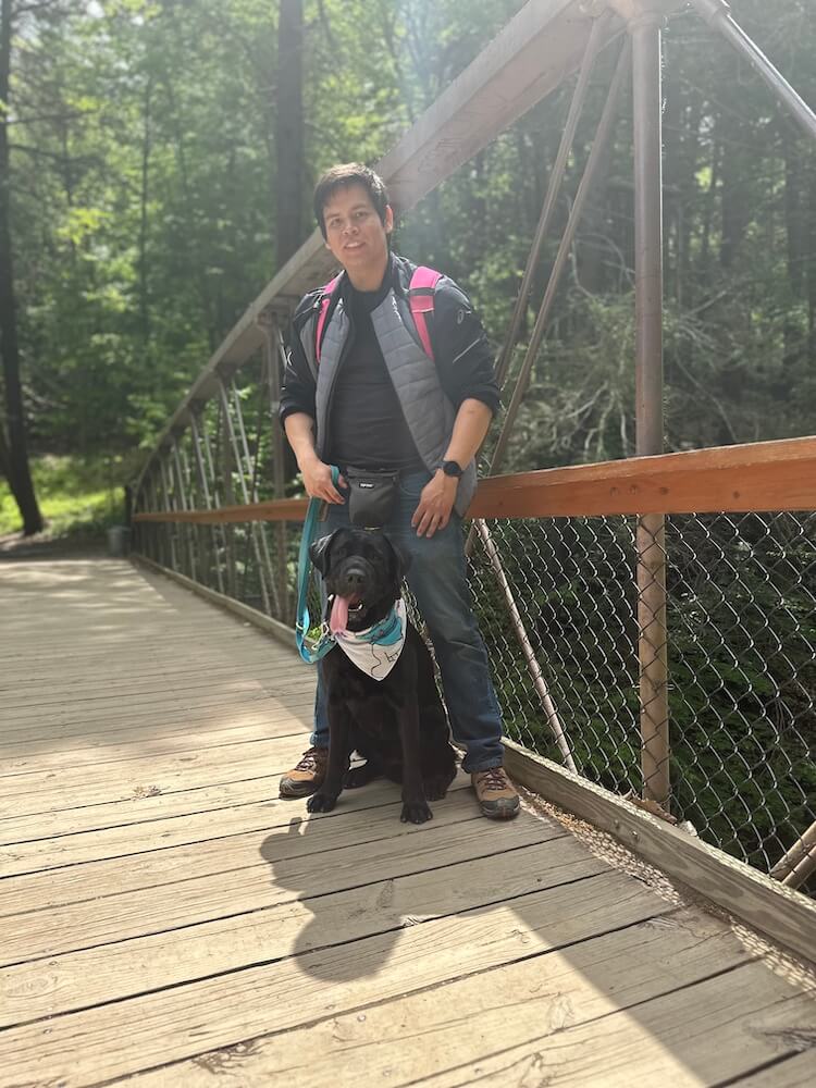 Pup on program Irving sits on a wooden bridge while hiking with his raiser Brandon