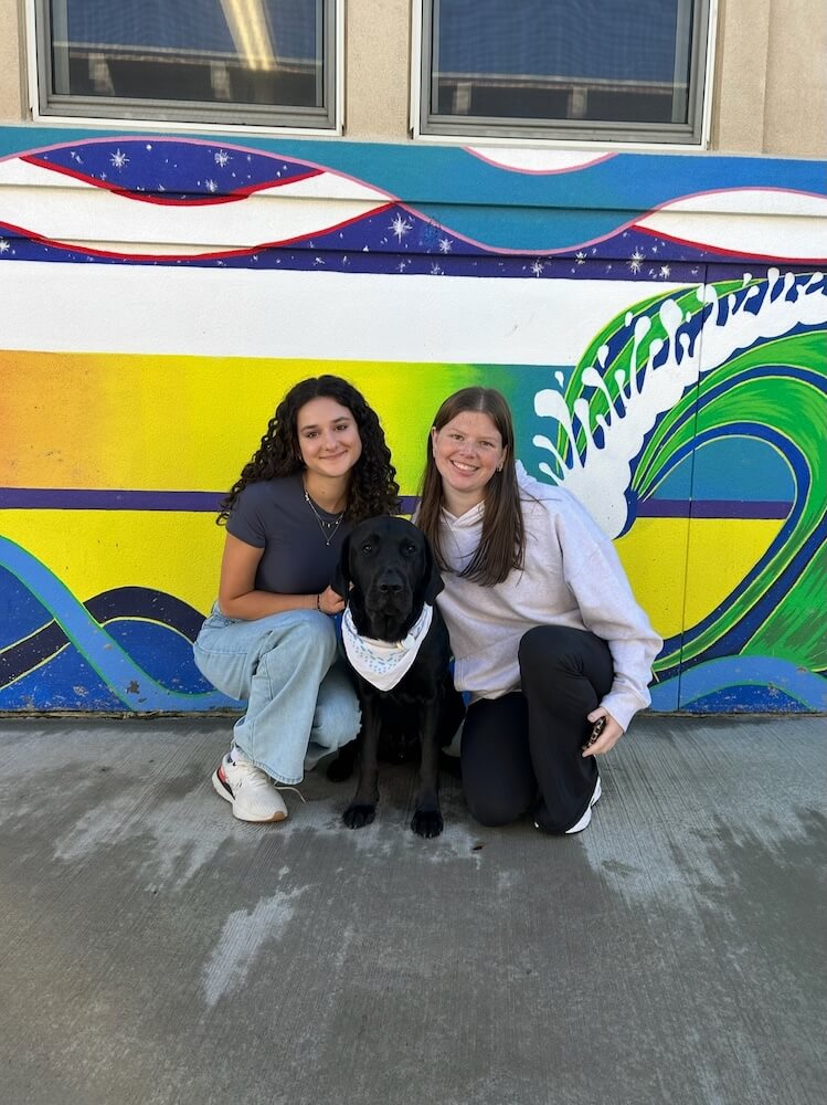 Pup on program Yodel with his two raisers in front of a colorful mural