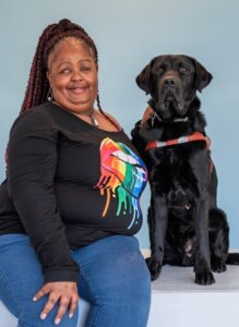 Nicole and black Lab guide dog Everley, sit together against a pale blue background for their team portrait