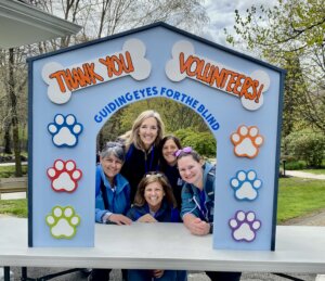 Five volunteers pose in the opening of a colorful doghouse structure that says Thank You Volunteers with pawprints
