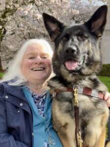 Zandra sits beside german shepherd guide dog Sedona in an outdoor shot for their team portrait