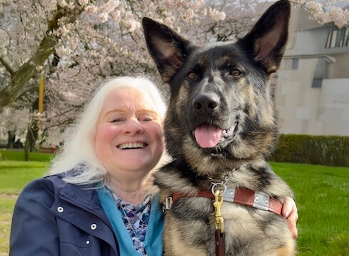 Zandra sits beside german shepherd guide dog Sedona in an outdoor shot for their team portrait