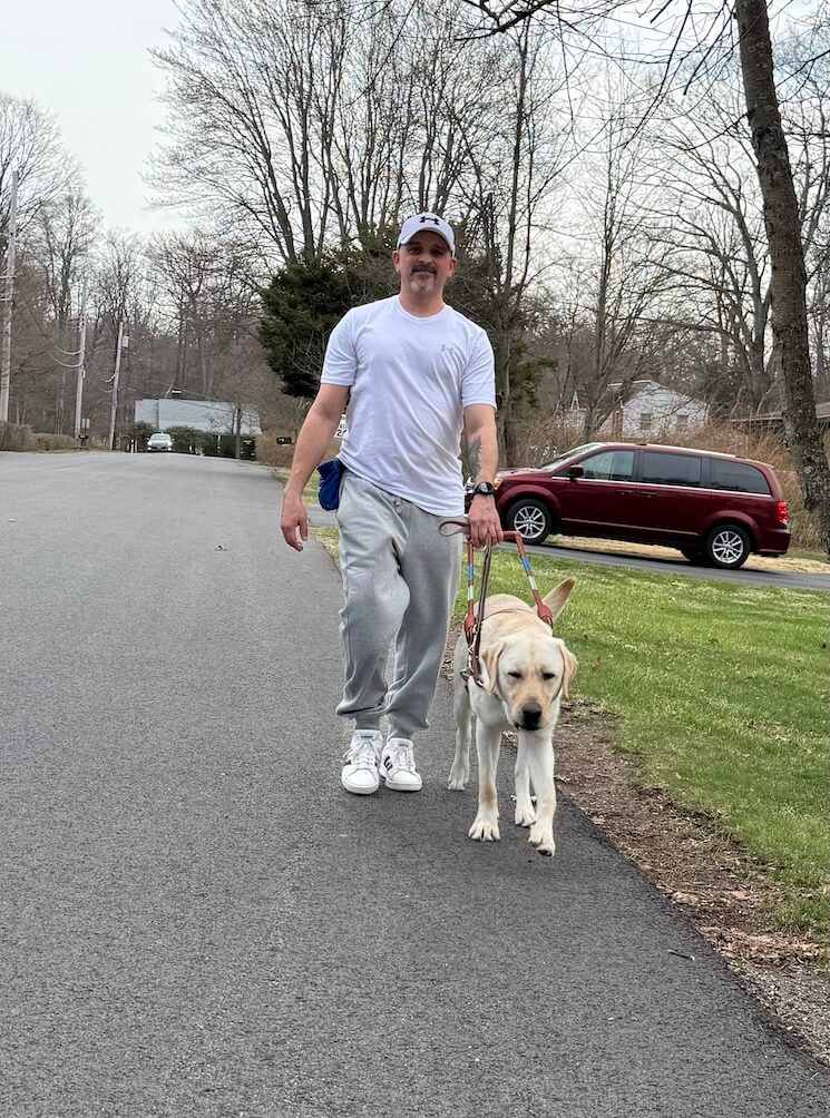 Brian and Moose walk towards the camera as they practice "shorelining" on a paved road lined in grassy yards