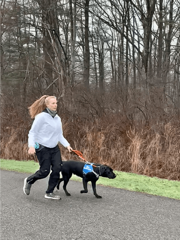 Christine and Vader run on pavement in wooded park with her ponytail swinging behind her.