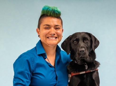 Damien and black Lab guide dog Whim pose for their graduate team portrait against a blue background.
