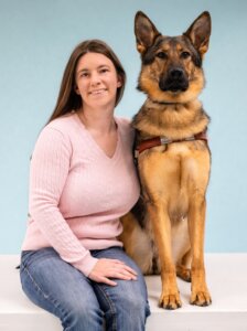 Meagan and German Shepherd Guide Dog Rhiana pose for their graduate portrait in front of a light blue background