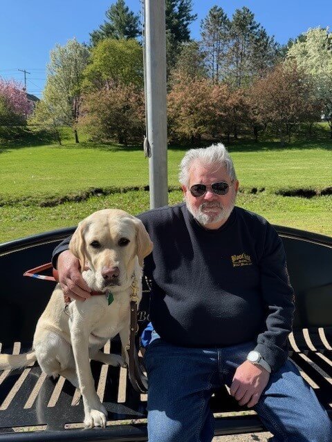 Paul sits outside with his arm around yellow Lab guide dog Abilene for their team portrait