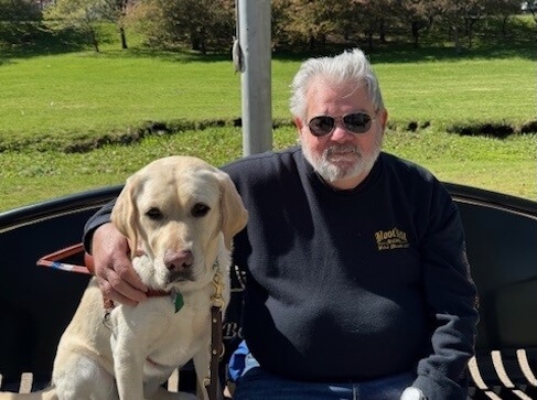 Paul sits outside with his arm around yellow Lab guide dog Abilene for their team portrait