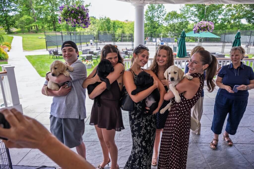 attendees with R26 puppies Rascal (male yellow), Robin (black female), Rajah (black male), and Rodeo (yellow male)
