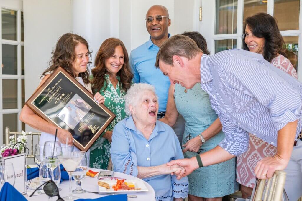 Eli greets wife of Al Maiolo as Al's 4 daughters happily watch along with Chris. One holds a lifetime achievement award plaque presented in honor of Al who passed away earlier this year. Al was a longtime friend and supporter of Guiding Eyes and an integral part of our annual golf event.