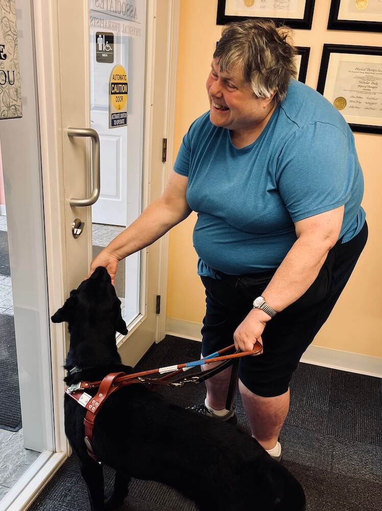 Katherine happily rewards guide dog Morgan with a treat at the entrance to PT services