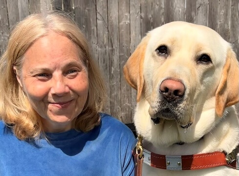 Tracy and yellow Lab Camden sit head to head on a sunny outdoor bench in front of a weathered fence