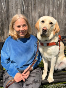 Tracy and yellow Lab Camden sit head to head on a sunny outdoor bench in front of a weathered fence