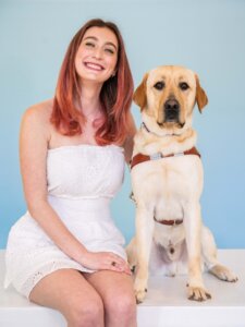 Annalisa and yellow Lab guide dog Vernon sit side by side for their team portrait against a blue background