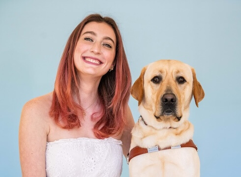 Annalisa and yellow Lab guide dog Vernon sit side by side for their team portrait against a blue background