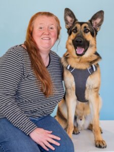 Christina and black & tan German Shepherd guide dog Zeppelin pose against a light blue background for their team portrait